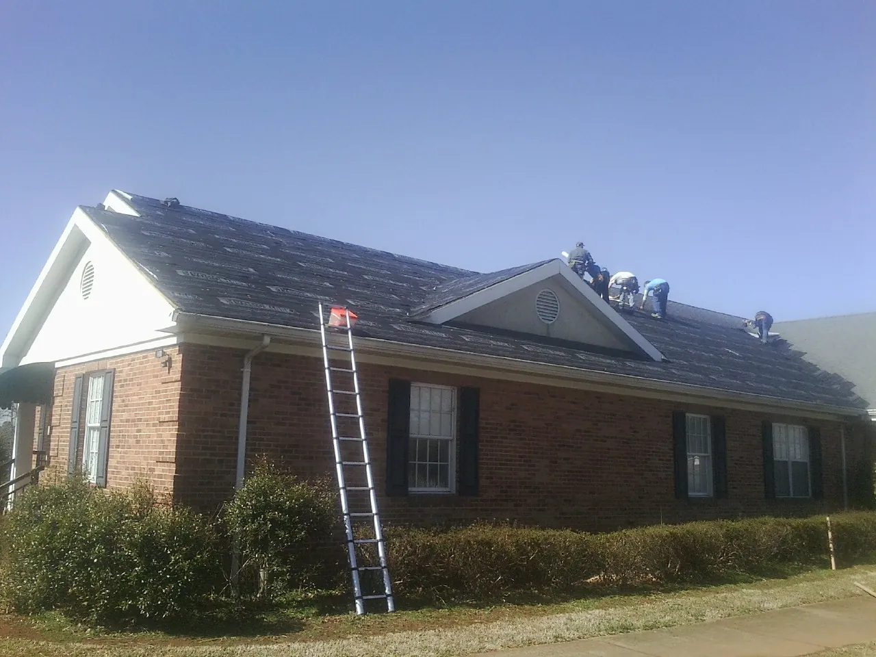 Crew tearing shingles off a brick ranch roof with a ladder set — Metal Roof Repair work by our crew in Warsaw