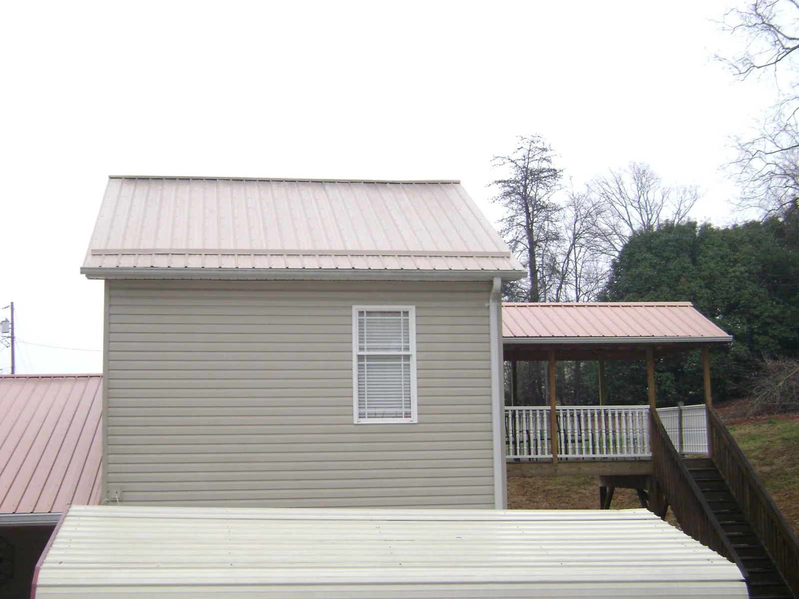 Tan metal roofs on a two story addition and attached porch, from a Roof Replacement job in Warsaw